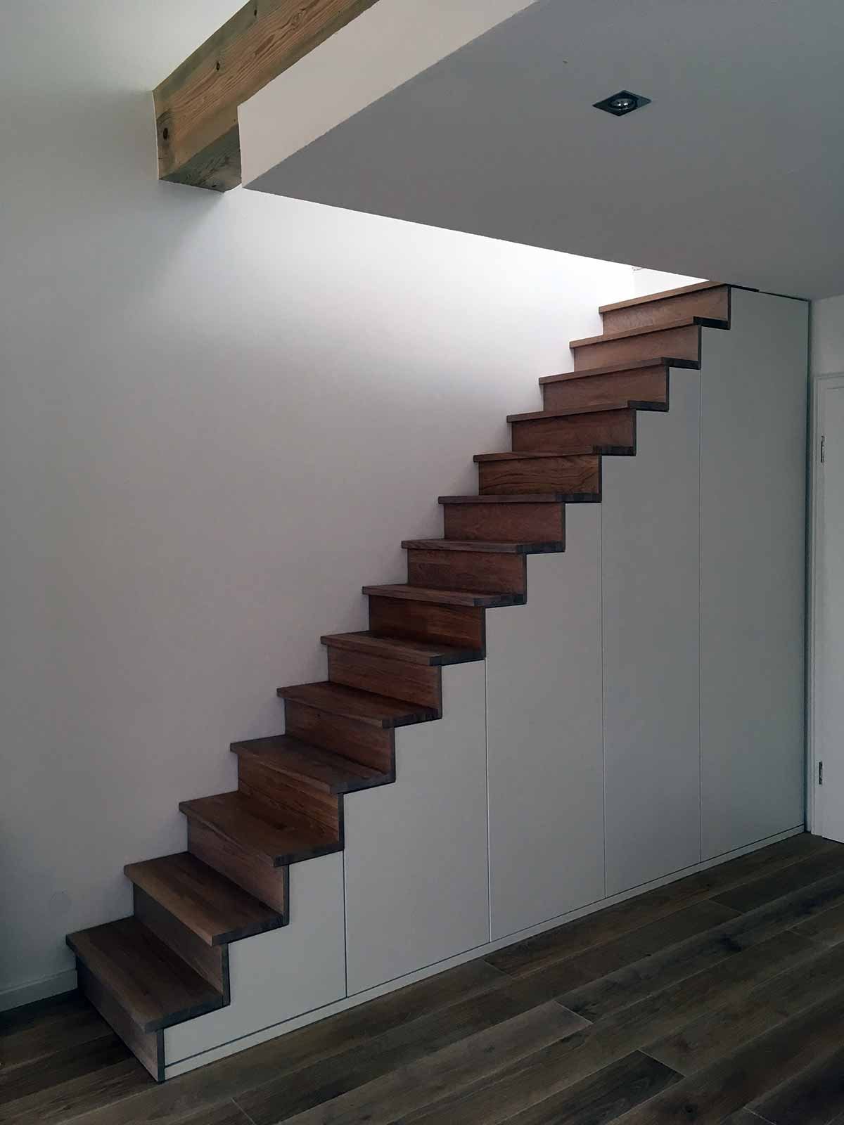 Gerade Treppe mit dunklen Holzstufen und weißen Schranktüren unter der Treppe